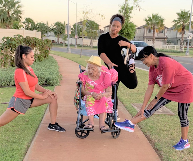 Relana, Carlina, Anaia and Menia stretch on a sidewalk during a training walk around a well-manicured neighborhood