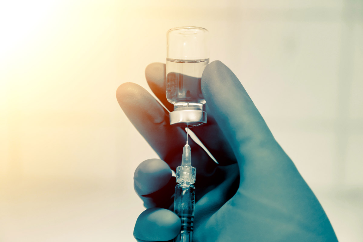 a gloved doctor's hand holding a syringe and vaccine vile