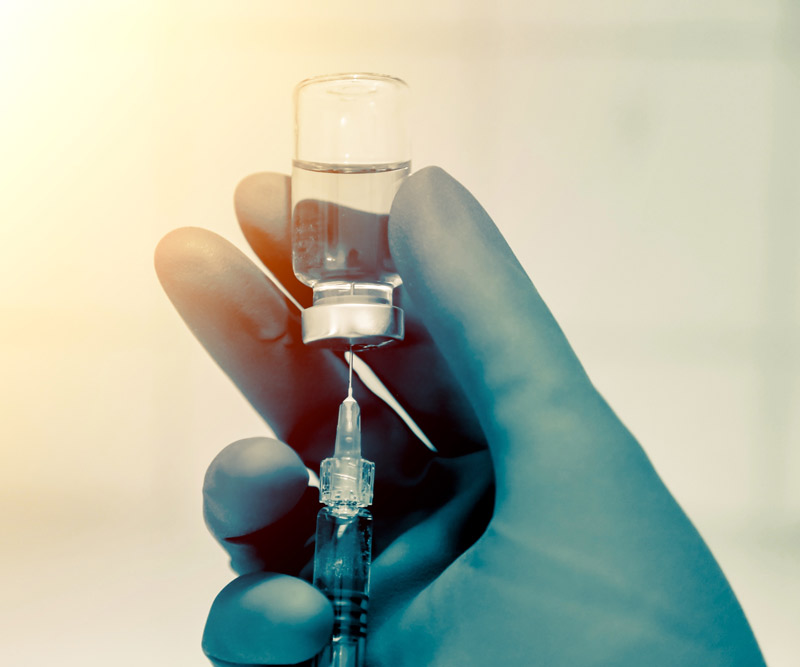 a gloved doctor's hand holding a syringe and vaccine vile