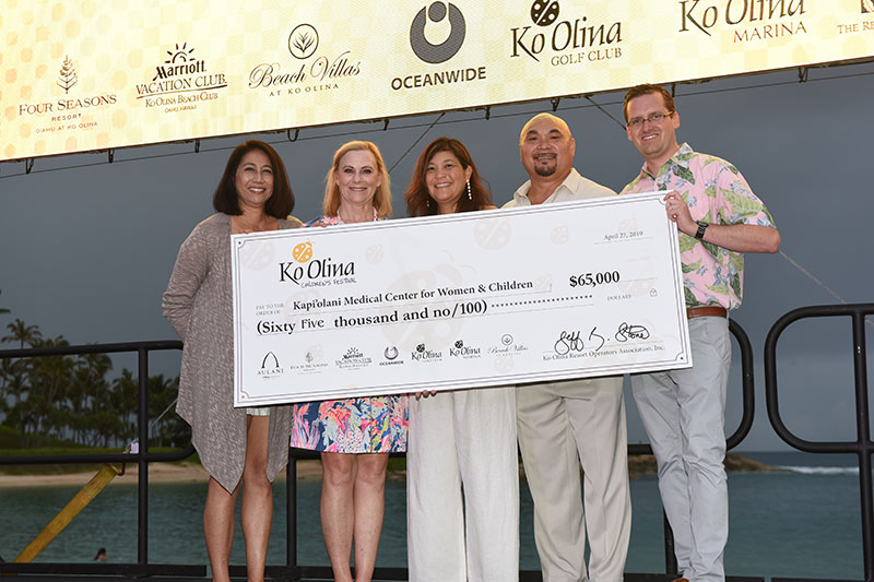 Three women and two men on stage holding ceremonial check for $65,000