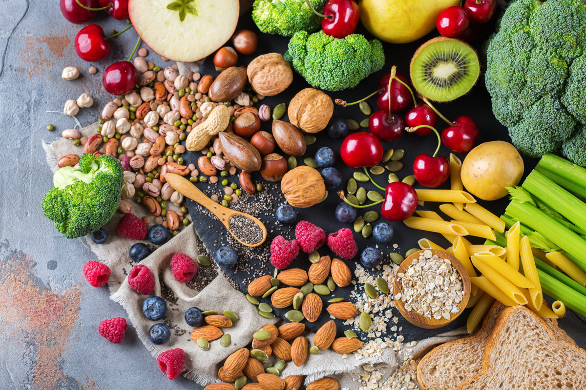 a variety of carb sources, including broccoli, berries, almonds, pumpkin seeds, chia seeds, cherries, apples, oatmeal, bread, legumes and pasta arranged on a slate counter