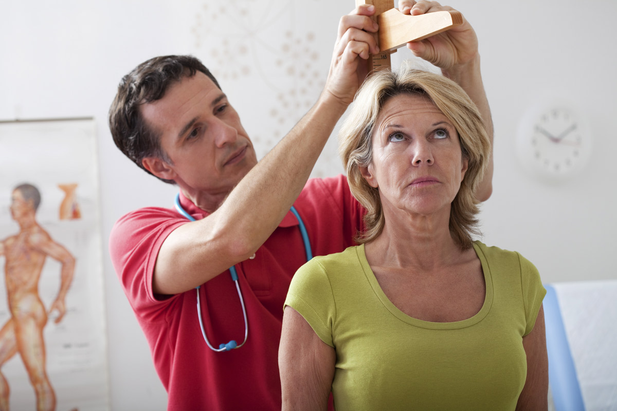 elderly woman having height measured by male nurse at the doctors' office