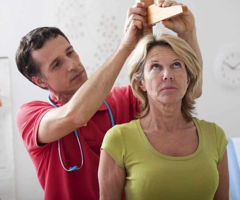 elderly woman having height measured by male nurse at the doctors' office