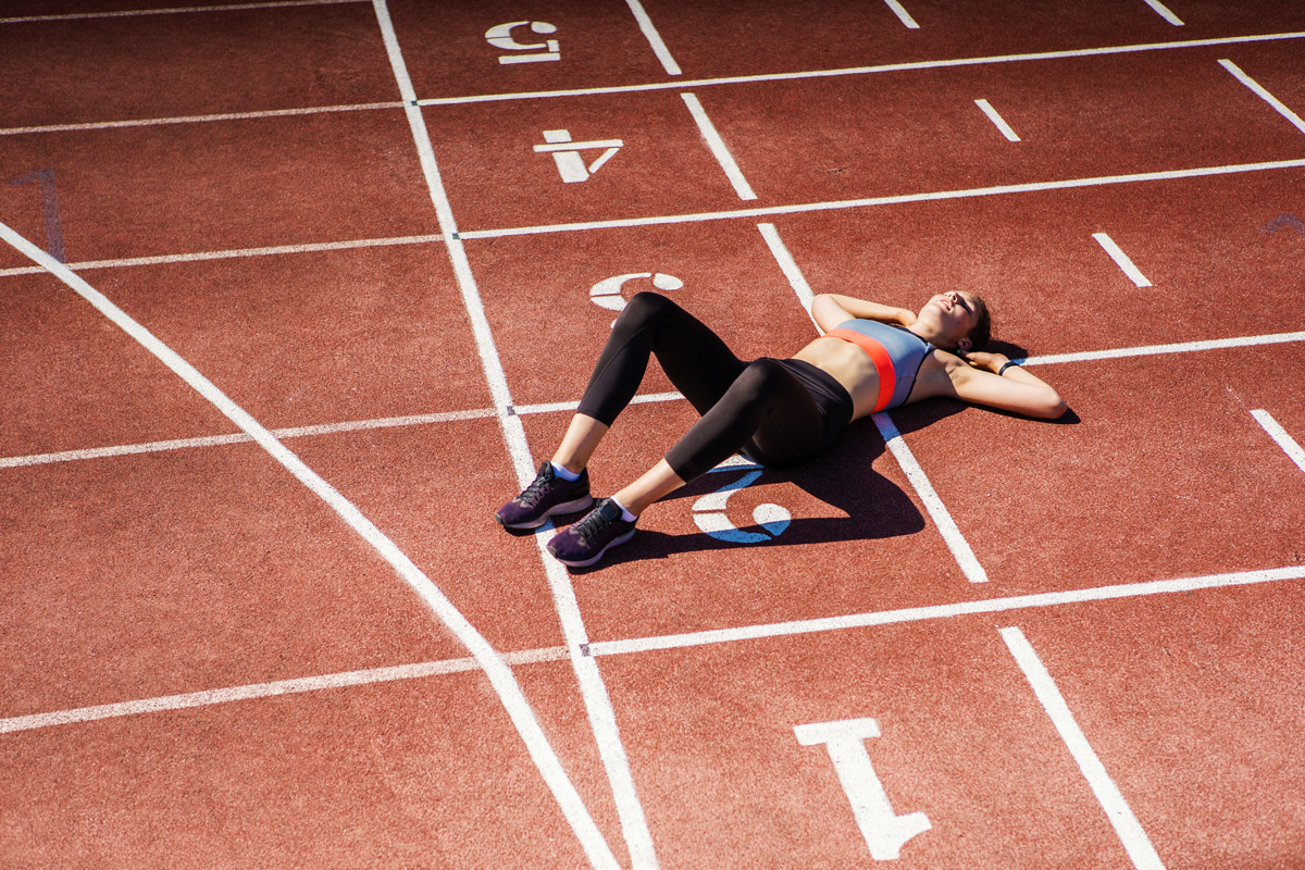 female athlete showing exhaustion by laying down on an outdoor running track