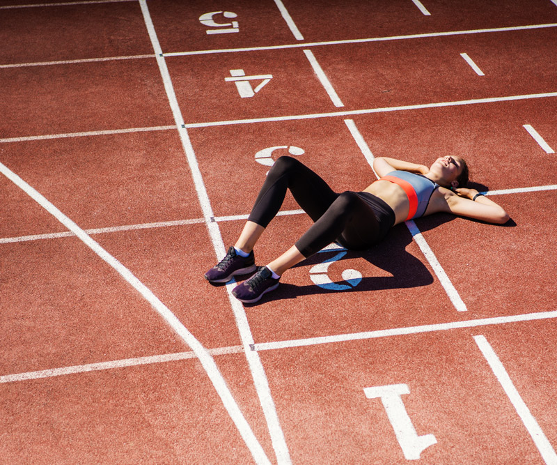 female athlete showing exhaustion by laying down on an outdoor running track