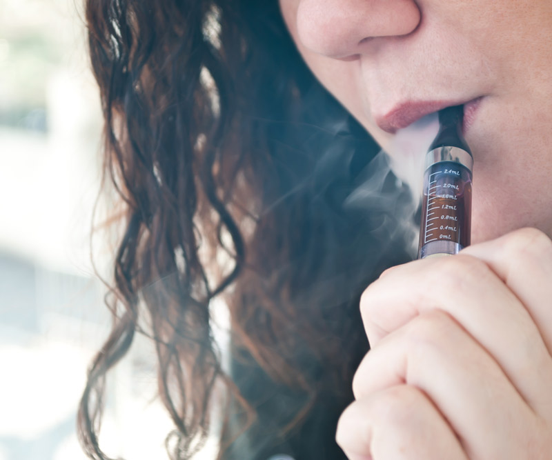 closeup of young woman taking a hit from an electronic smoking device with smoke swirling around her head