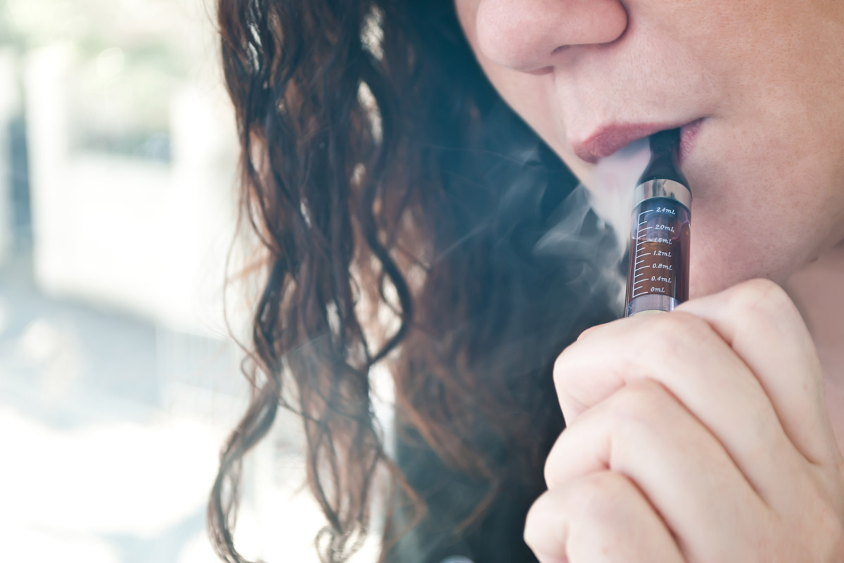 closeup of young woman taking a hit from an electronic smoking device with smoke swirling around her head