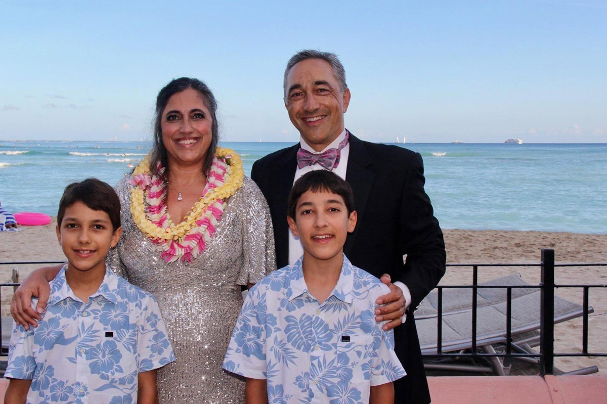 a man and woman with their two young boys stand on the balcony of a beachfront hotel in Hawaii