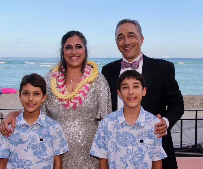 a man and woman with their two young boys stand on the balcony of a beachfront hotel in Hawaii
