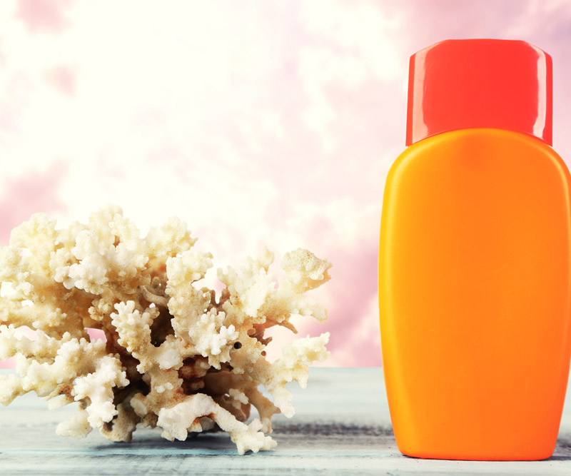 an orange bottle of sunscreen on a table next to a piece of coral