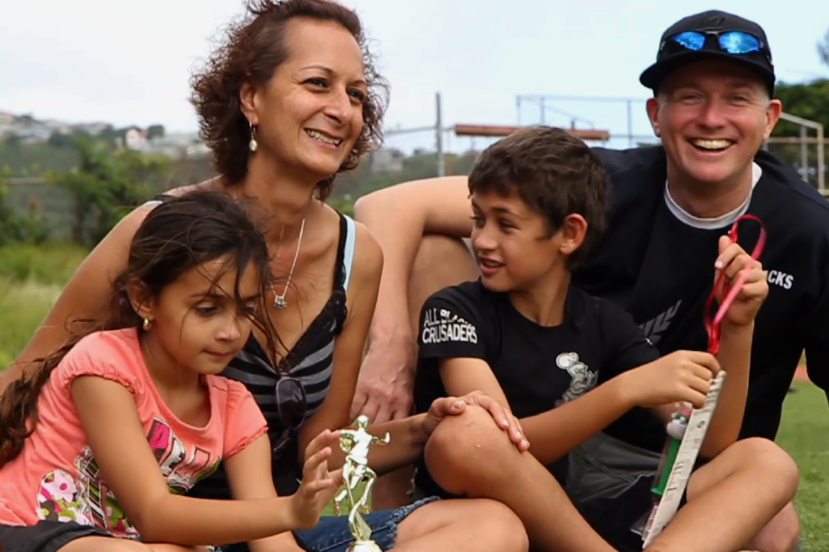 Shanti Woodrow and family; a husband a wife sitting on the grass of a baseball field with their son and daughter