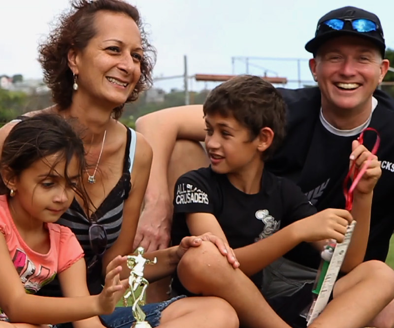 Shanti Woodrow and family; a husband a wife sitting on the grass of a baseball field with their son and daughter