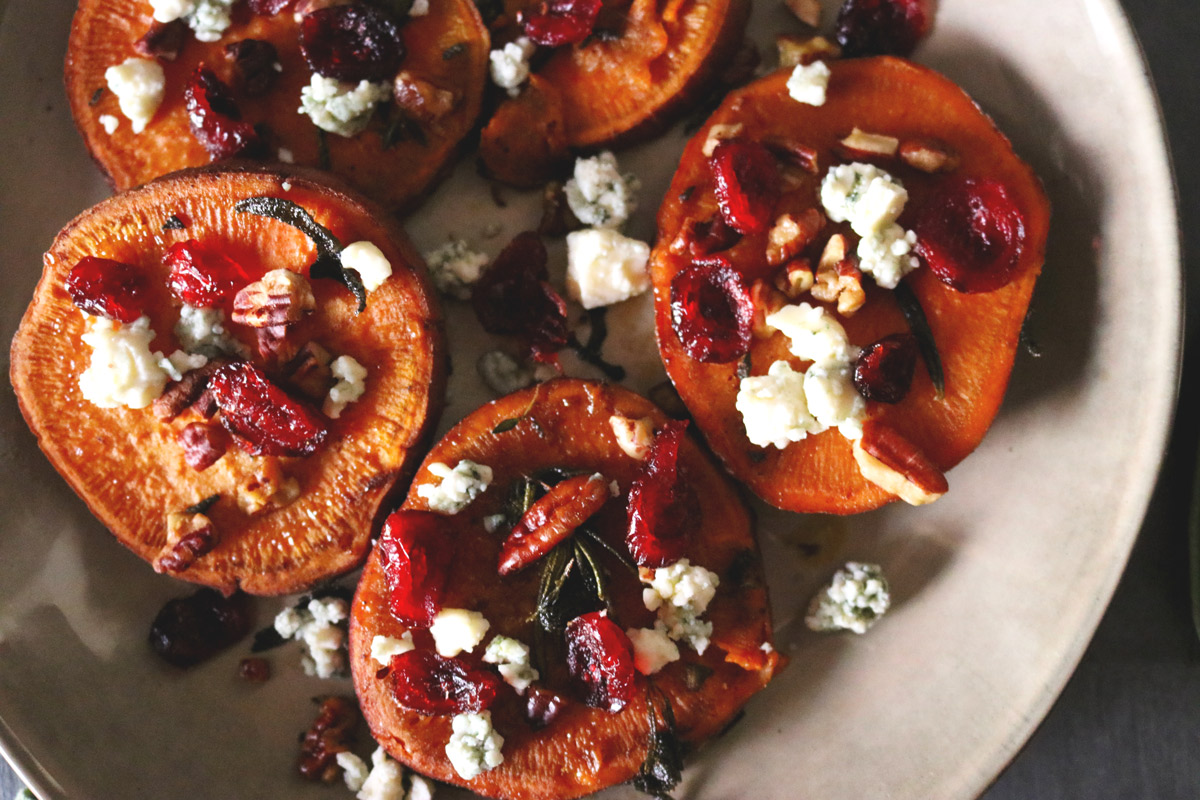 a plate of sliced sweet potato rounds topped with crumbled blue cheese, chopped pecans and dried cranberries