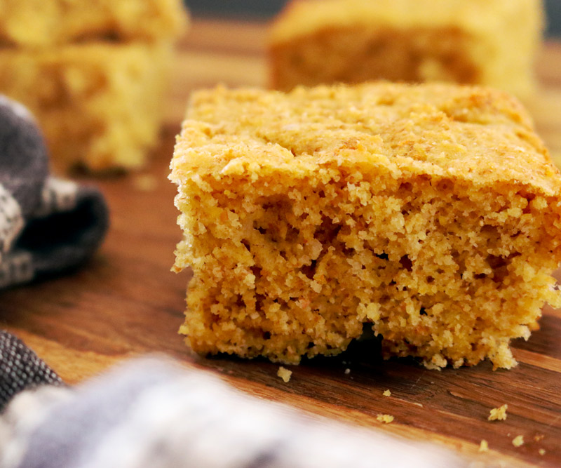 closeup of cornbread slices on a wooden butcher block counter with a dark-grey hand towel placed off to the side