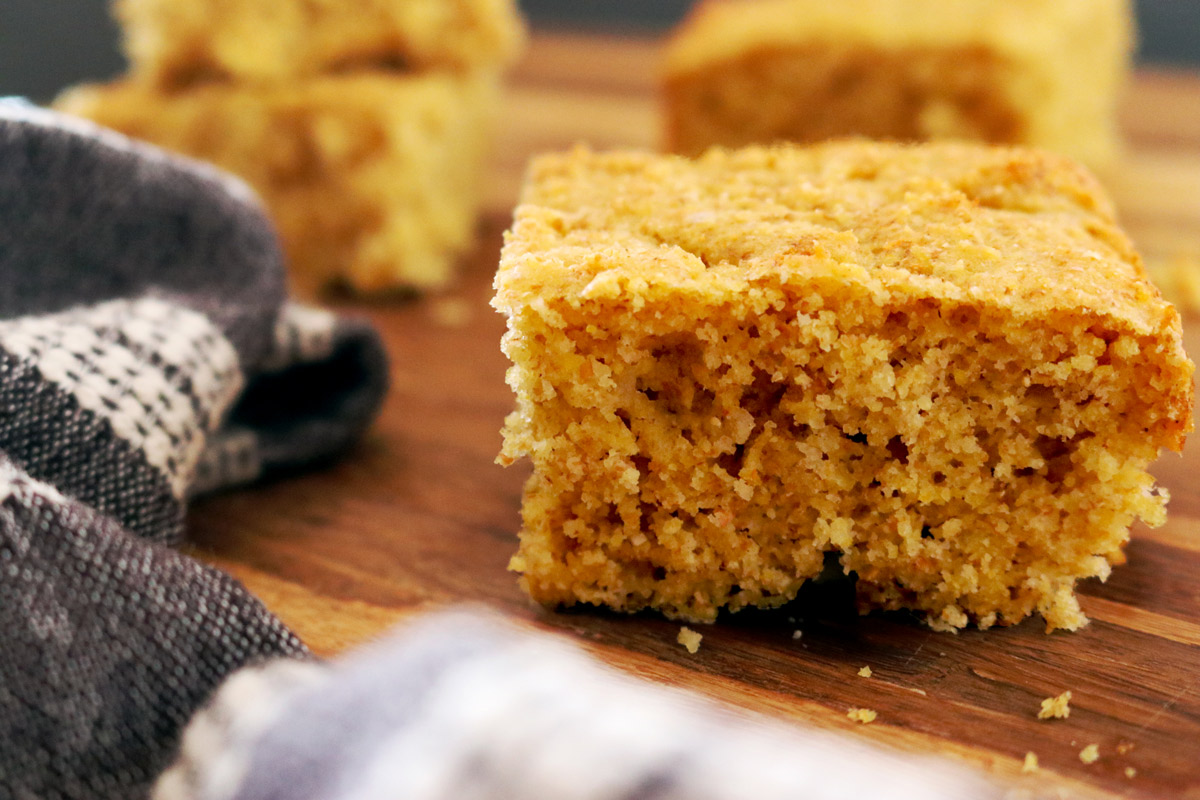 closeup of cornbread slices on a wooden butcher block counter with a dark-grey hand towel placed off to the side