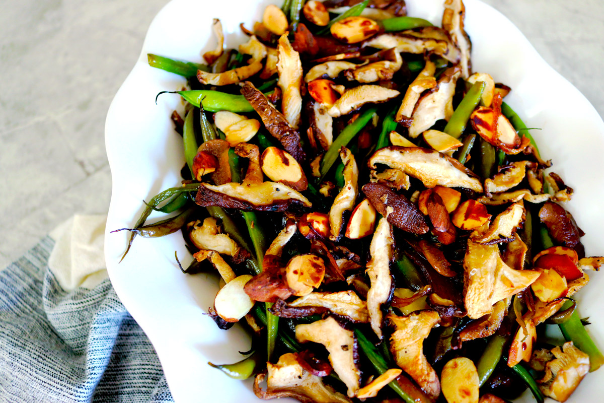 a white serving plate of Garlicky Green Beans topped with crispy mushrooms and almonds