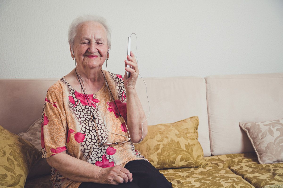old woman sitting on couch listening to music from a mobile phone
