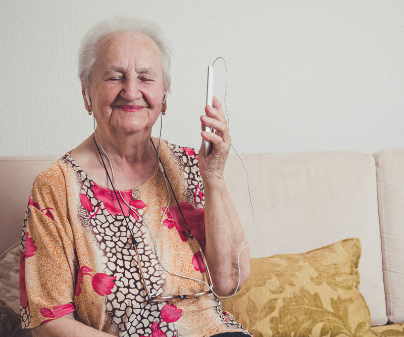 old woman sitting on couch listening to music from a mobile phone