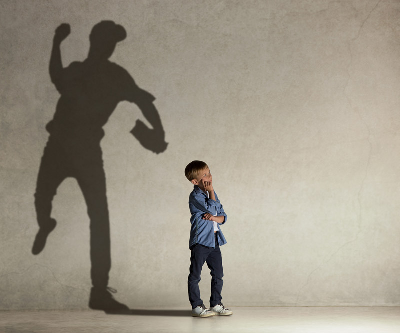 young boy looking off into the distance thinking with a shadow of a professional baseball player behind him to signify his dreams of playing in the Major Leagues