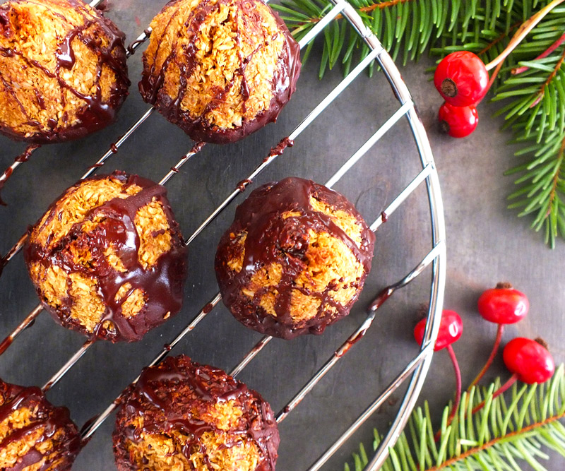 Dark Chocolate-Dipped Mint Macaroon cookies rest on a wire rack on a slate counter top decorated with evergreen branches and holly