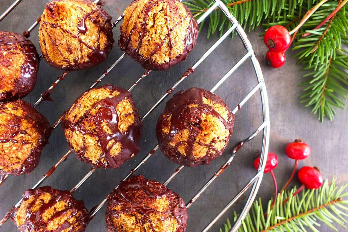 Dark Chocolate-Dipped Mint Macaroon cookies rest on a wire rack on a slate counter top decorated with evergreen branches and holly