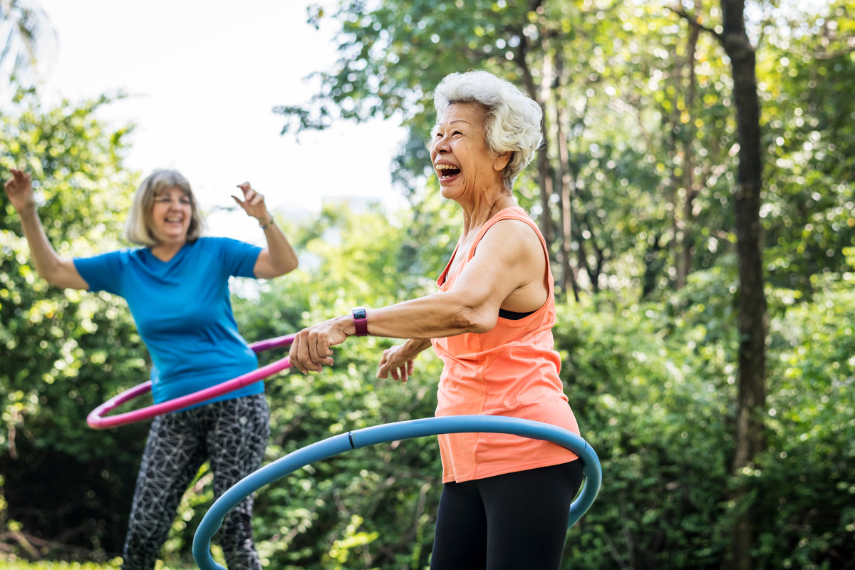 two elderly women happily laughing and playing with hula hoops outdoors