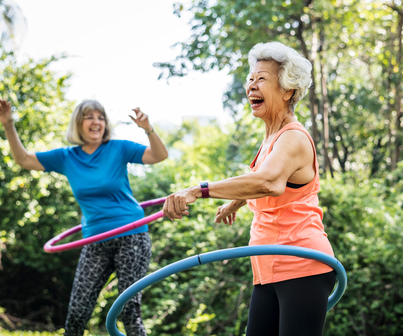 two elderly women happily laughing and playing with hula hoops outdoors