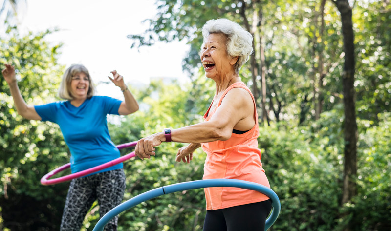 two elderly women happily laughing and playing with hula hoops outdoors