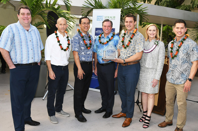 a group of people wearing lei stand in the Straub Rotunda holding a trophy