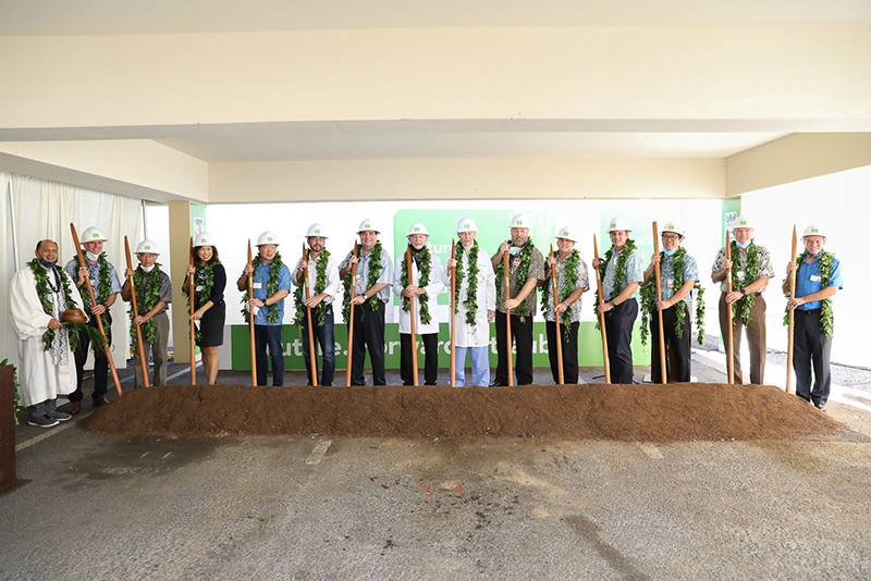 Group of people holding Hawaiian o'o sticks in dirt for groundbreaking ceremony
