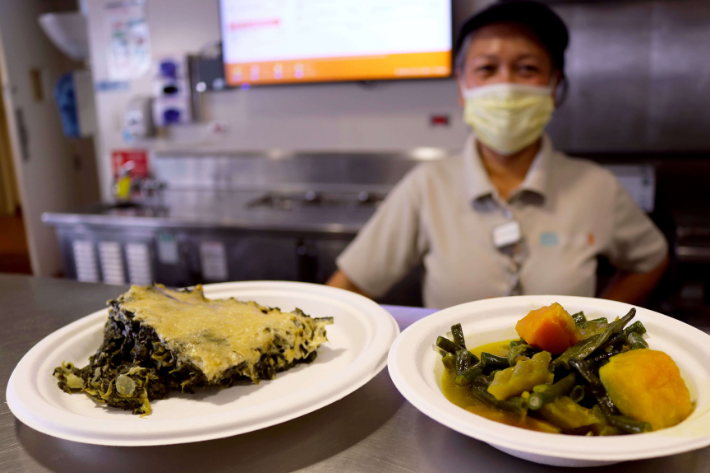 Cafe worker serving vegetarian spinach artichoke casserole and pinakbet