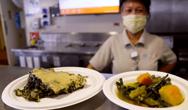 Cafe worker serving vegetarian spinach artichoke casserole and pinakbet