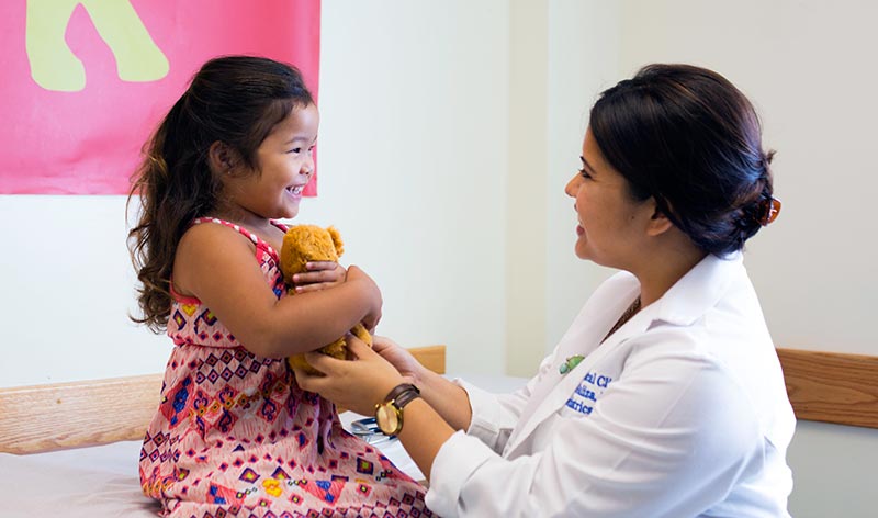 doctor with young patient holding a teddy bear in an exam room