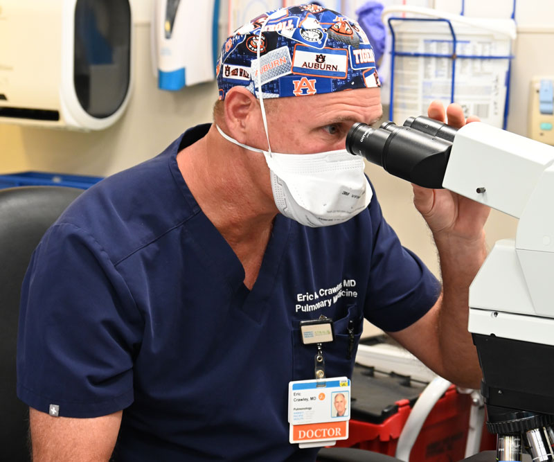 a doctor in scrubs looks into a microscope