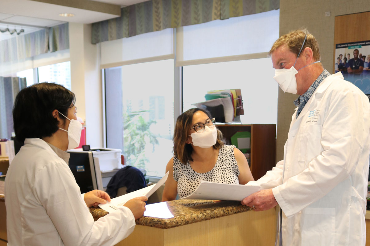 A female and male doctor and a female nurse talk around a table