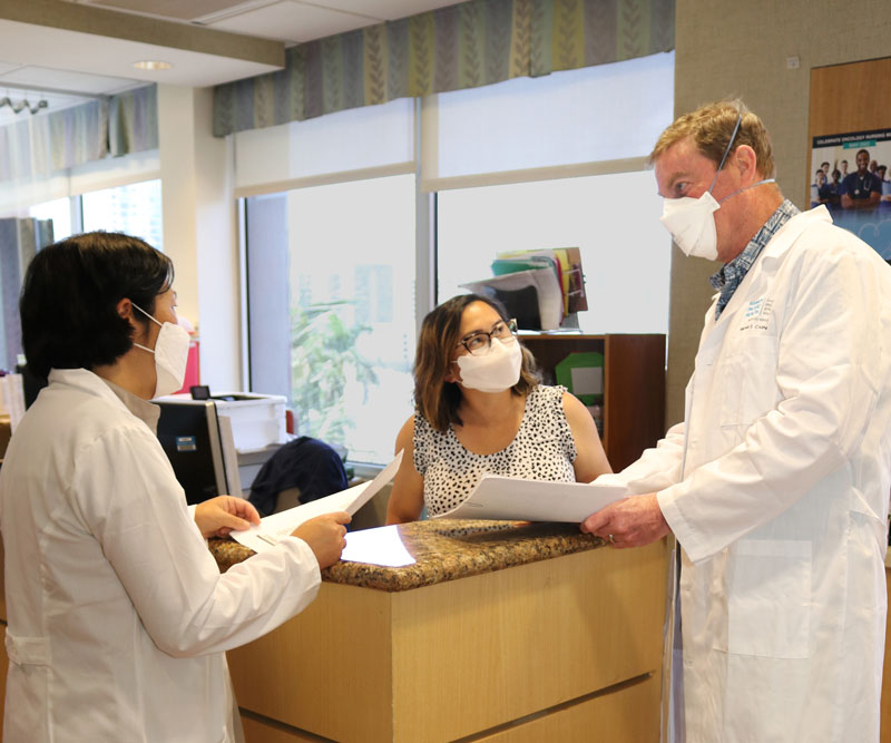 A female and male doctor and a female nurse talk around a table