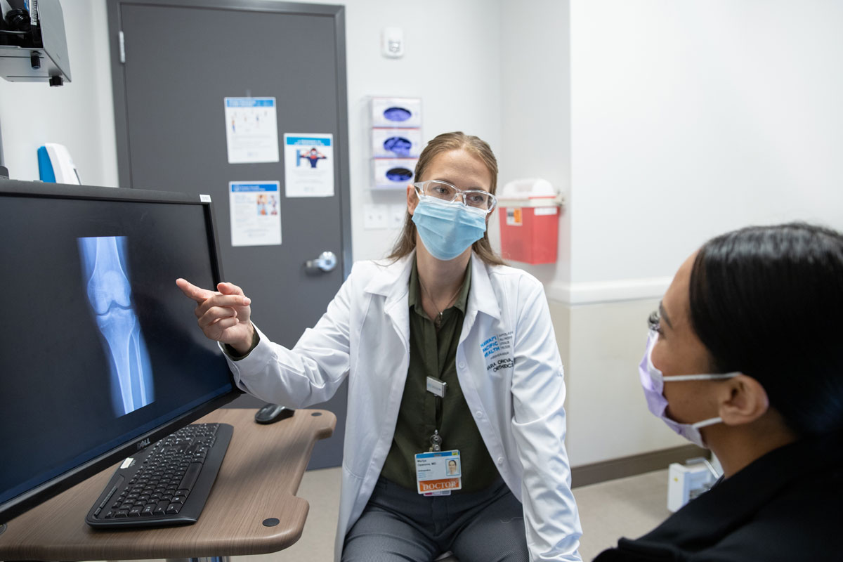 Orthopedic surgeon Dr. Mariya Opanova points to an X-ray while speaking with a female patient in an exam room.