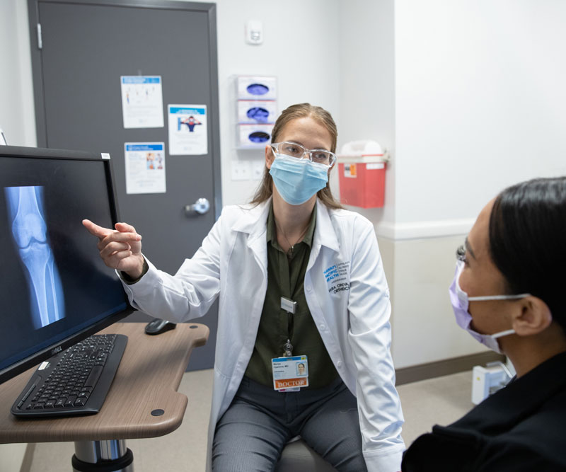 Orthopedic surgeon Dr. Mariya Opanova points to an X-ray while speaking with a female patient in an exam room.