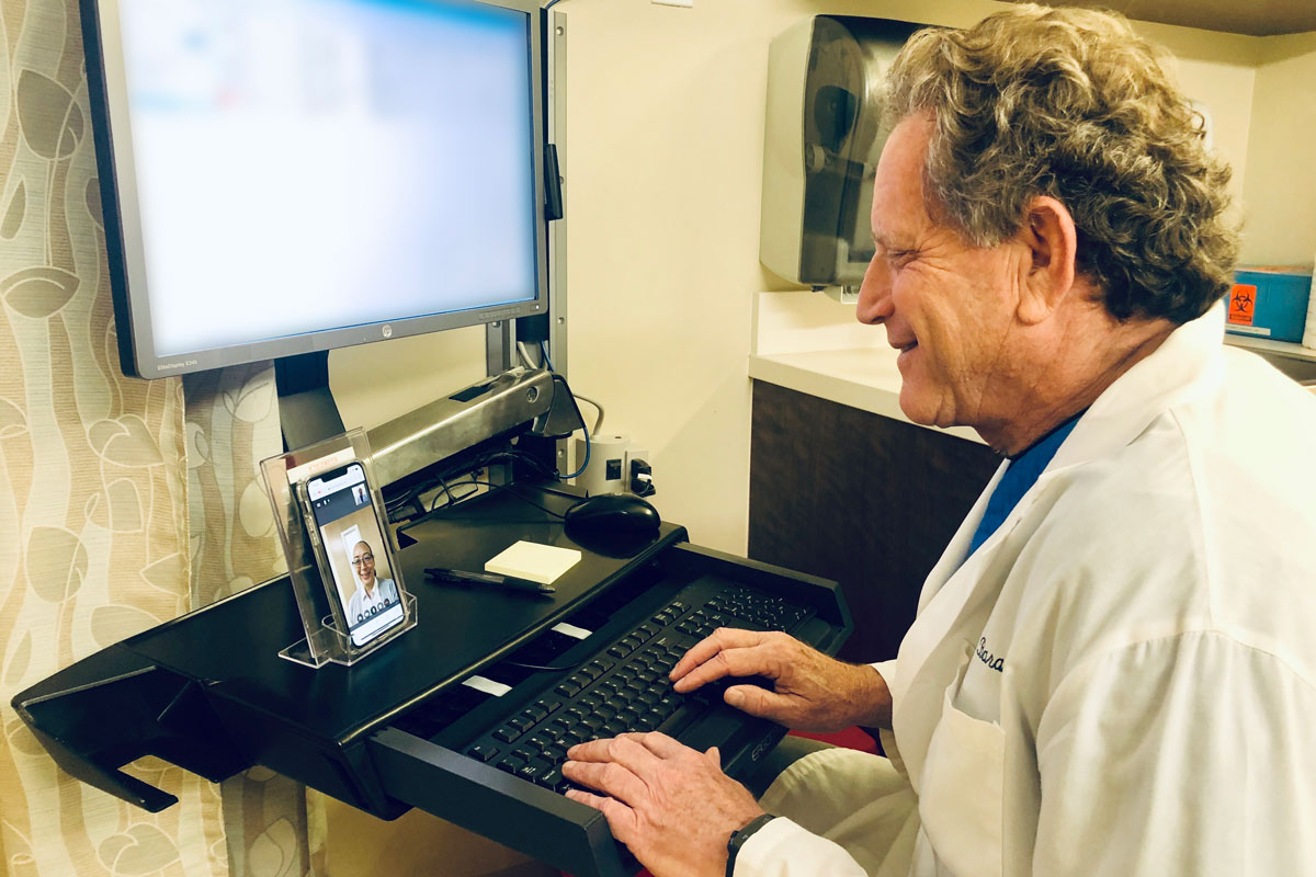 Dr. James Barahal sits at a computer and talks with a patient over a telehealth screen.