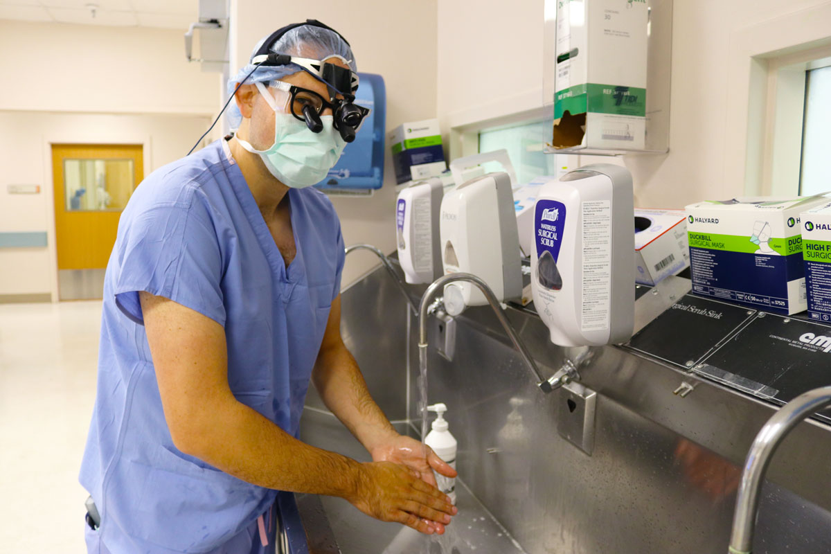 Dr. Louis Capecci wears surgical scrubs and washes his hands as he prepares for surgery in a hospital.