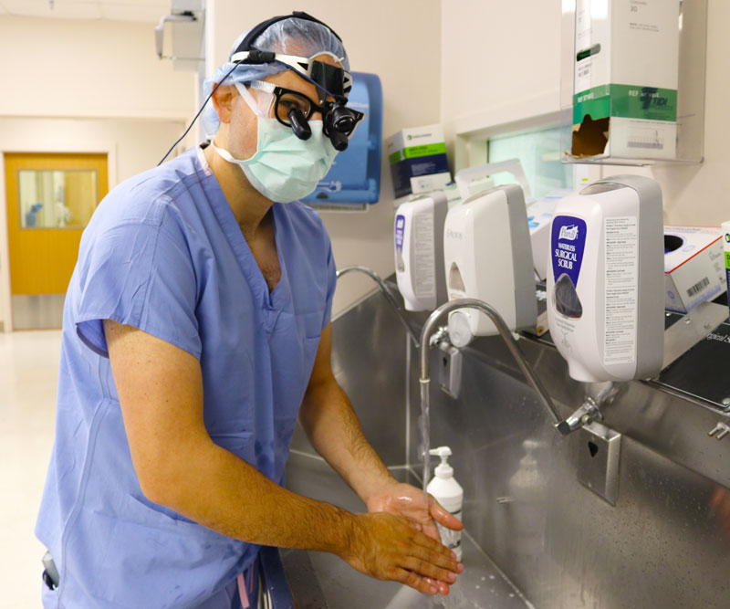 Dr. Louis Capecci wears surgical scrubs and washes his hands as he prepares for surgery in a hospital.