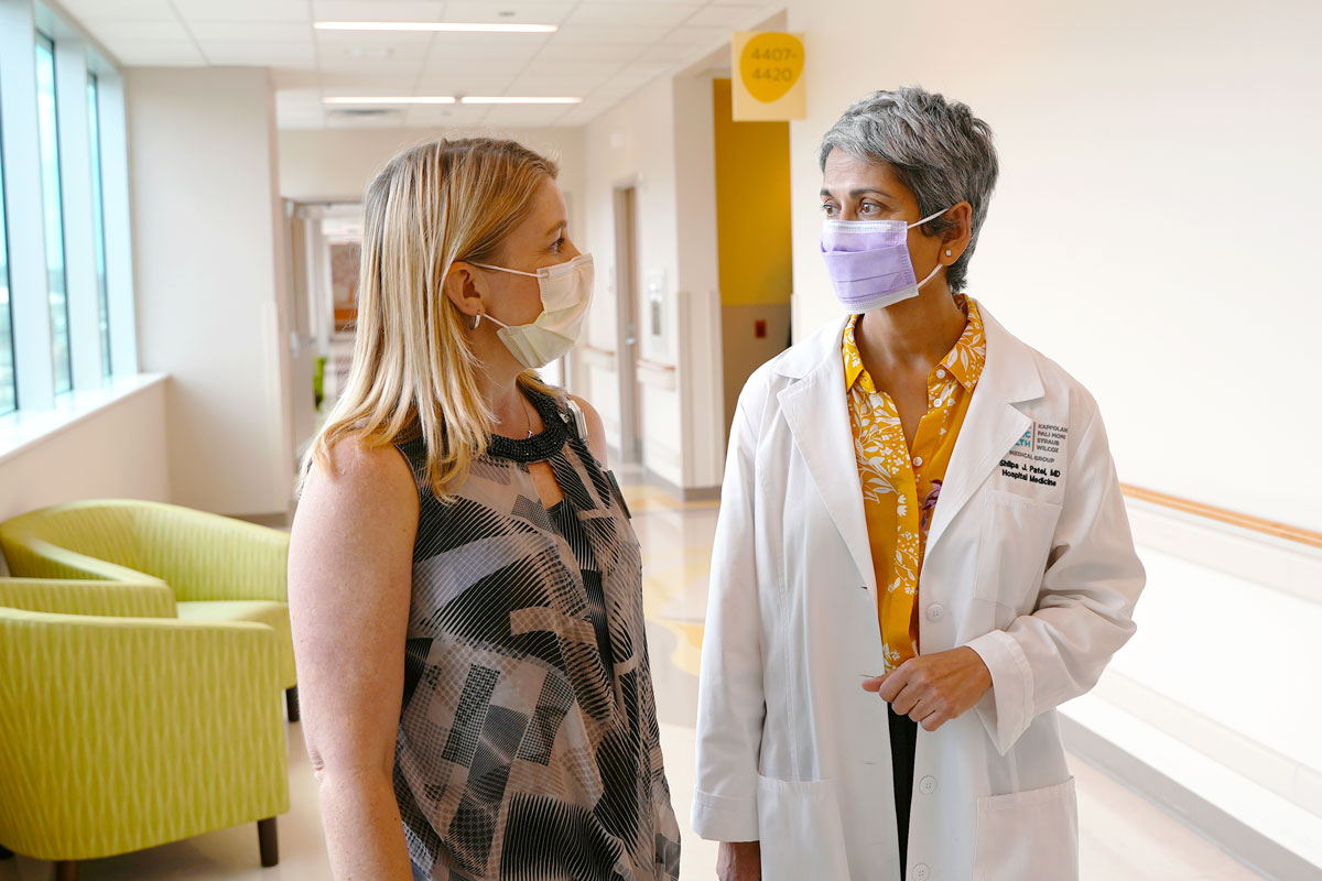 Two women walk through a brightly lit hall in a children's hospital, looking at each other and talking