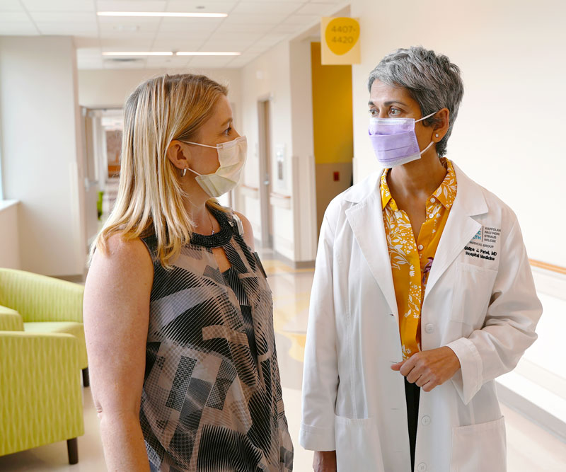 Two women walk through a brightly lit hall in a children's hospital, looking at each other and talking