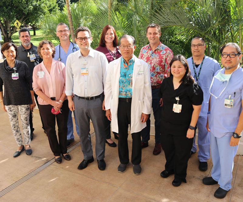 A group of doctors, nurses and hospital administrative staff smile at the camera for a group photo taken outside of a medical center in Hawaii