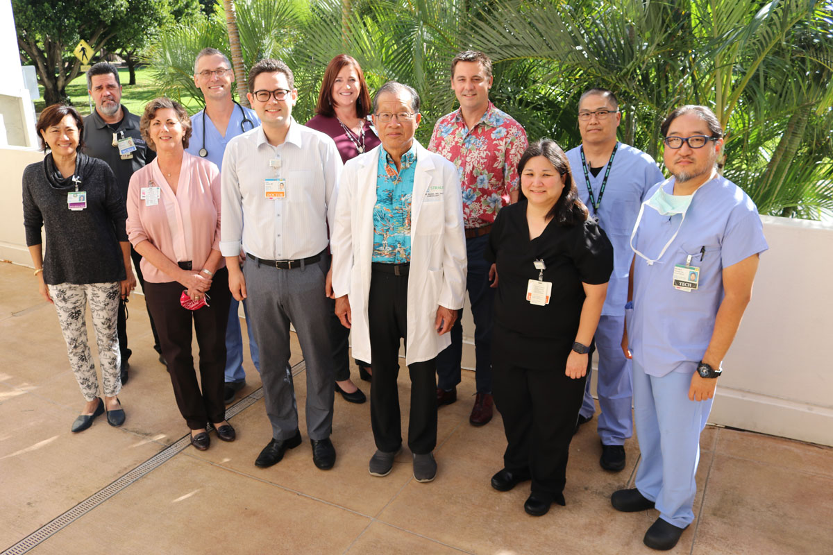A group of doctors, nurses and hospital administrative staff smile at the camera for a group photo taken outside of a medical center in Hawaii