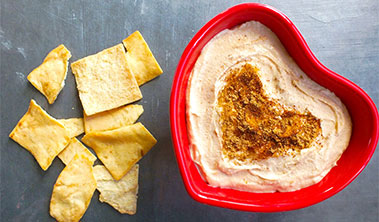 hummus in a heart shaped dish alongside pita chips