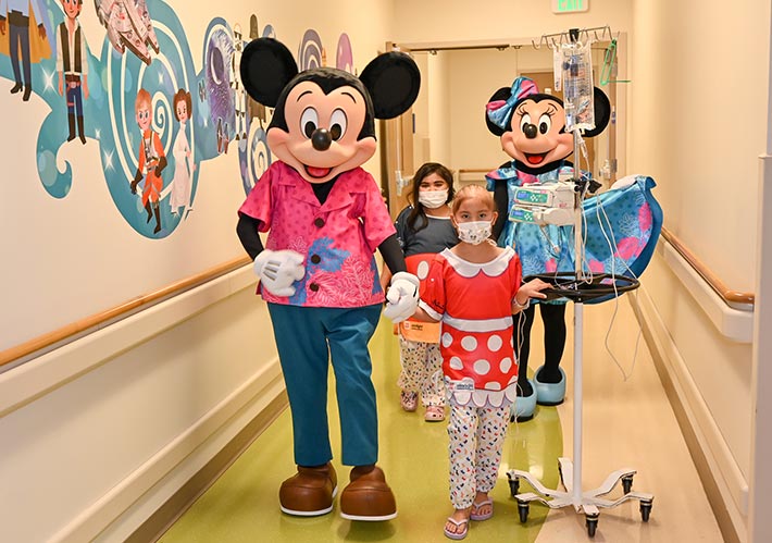 Two pediatric patients with Mickey & Minnie Mouse characters in a hospital hallway with a Disney mural