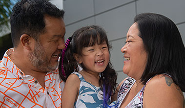 young smiling child embraced by her parents