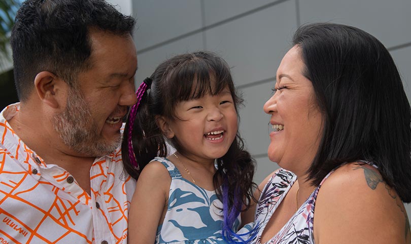 young smiling child embraced by her parents