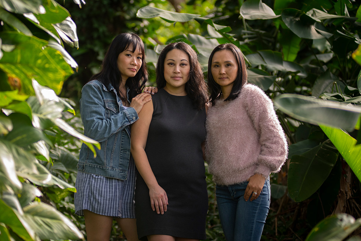 Three women stand closely together in a tropical rainforest.